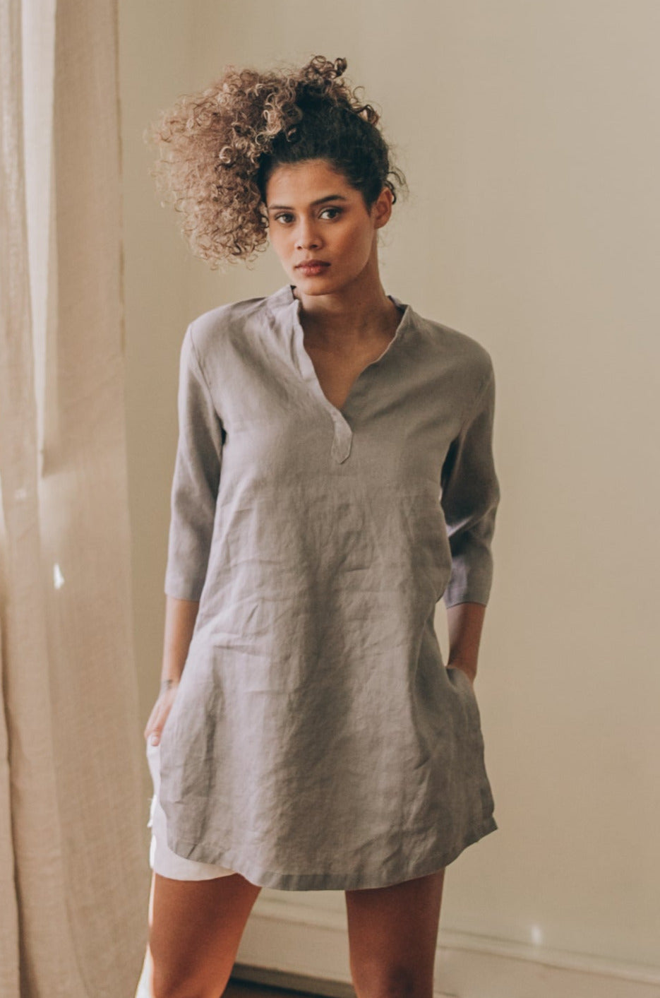 Woman wearing gray basic linen tunic shirt with split neckline and three-quarter sleeves indoors