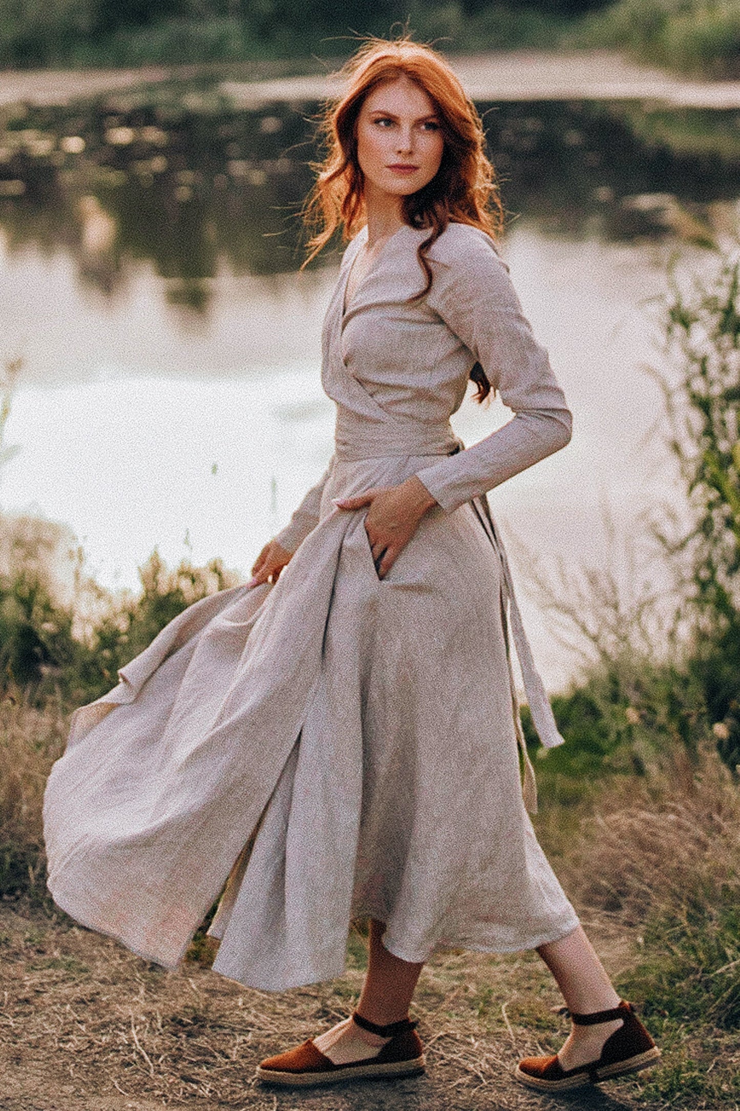 Woman wearing long sleeved linen wrap midi dress by lake in natural setting