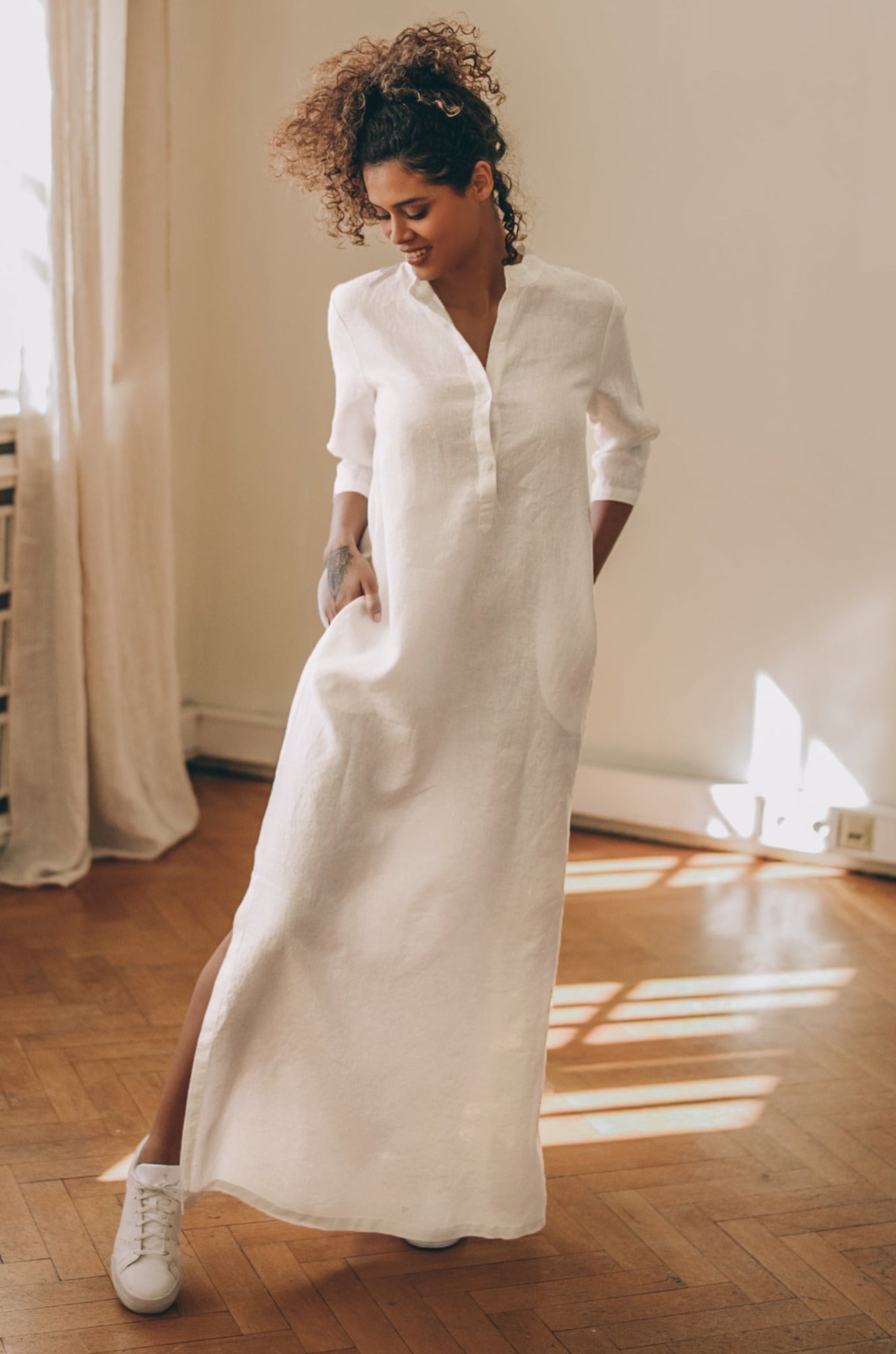 Woman wearing white 100% linen kaftan dress with elbow sleeves and side slits indoors