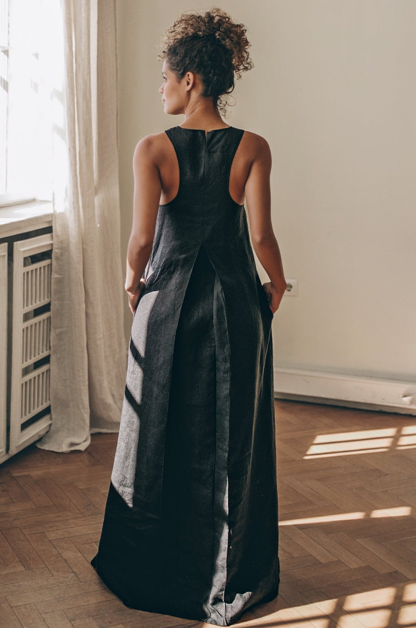 back view of sleeveless minimalist linen dress with pleat detail on model indoors