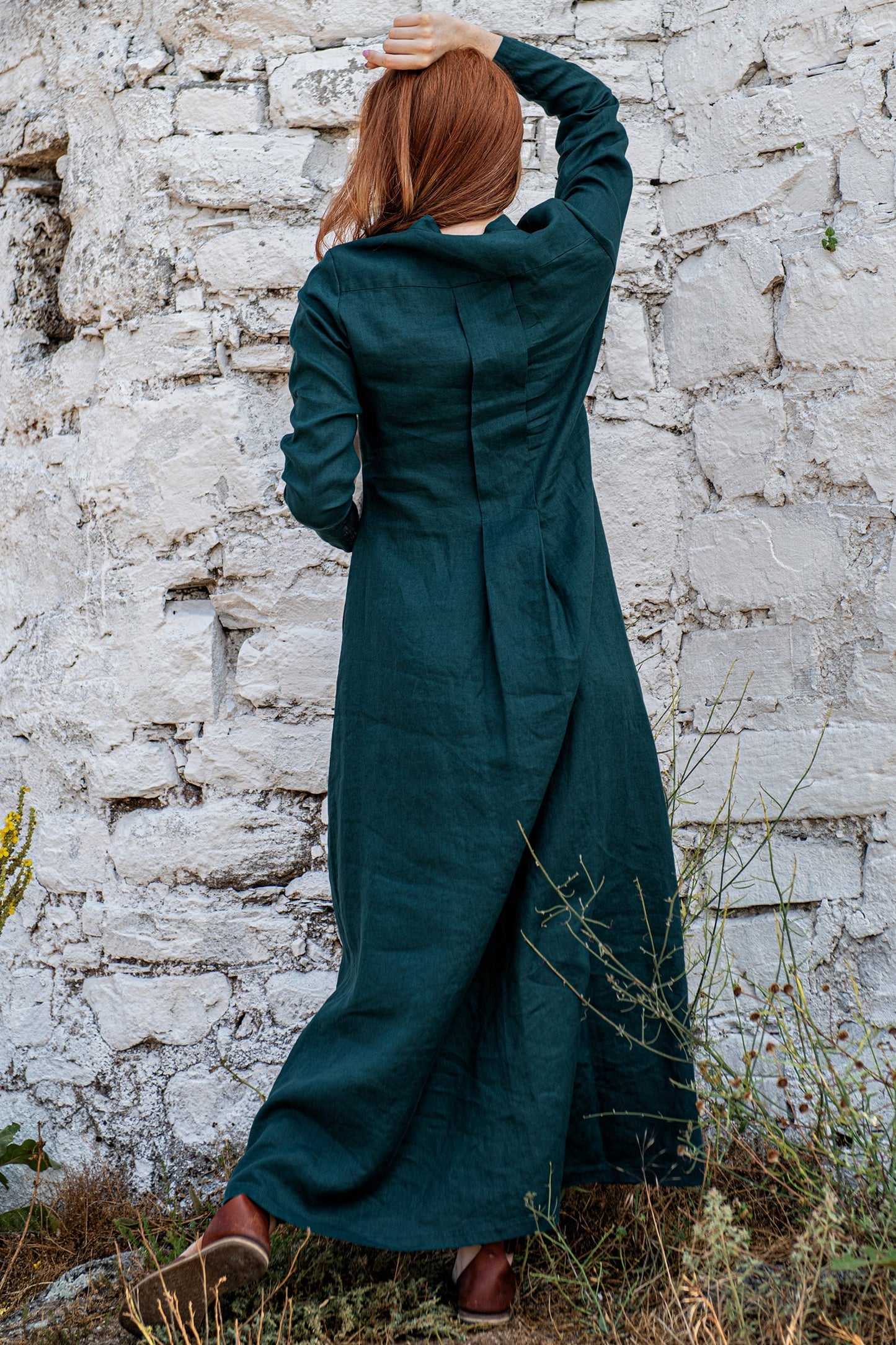 Back view of woman wearing dark green maxi linen shirt dress with full sleeves and slim fit silhouette outdoors