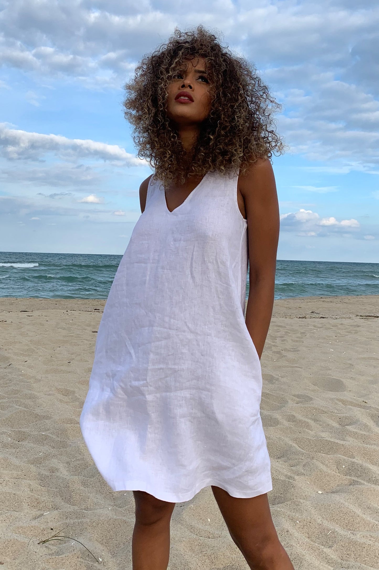 Woman wearing a breezy linen dress on the beach with a cloudy sky background