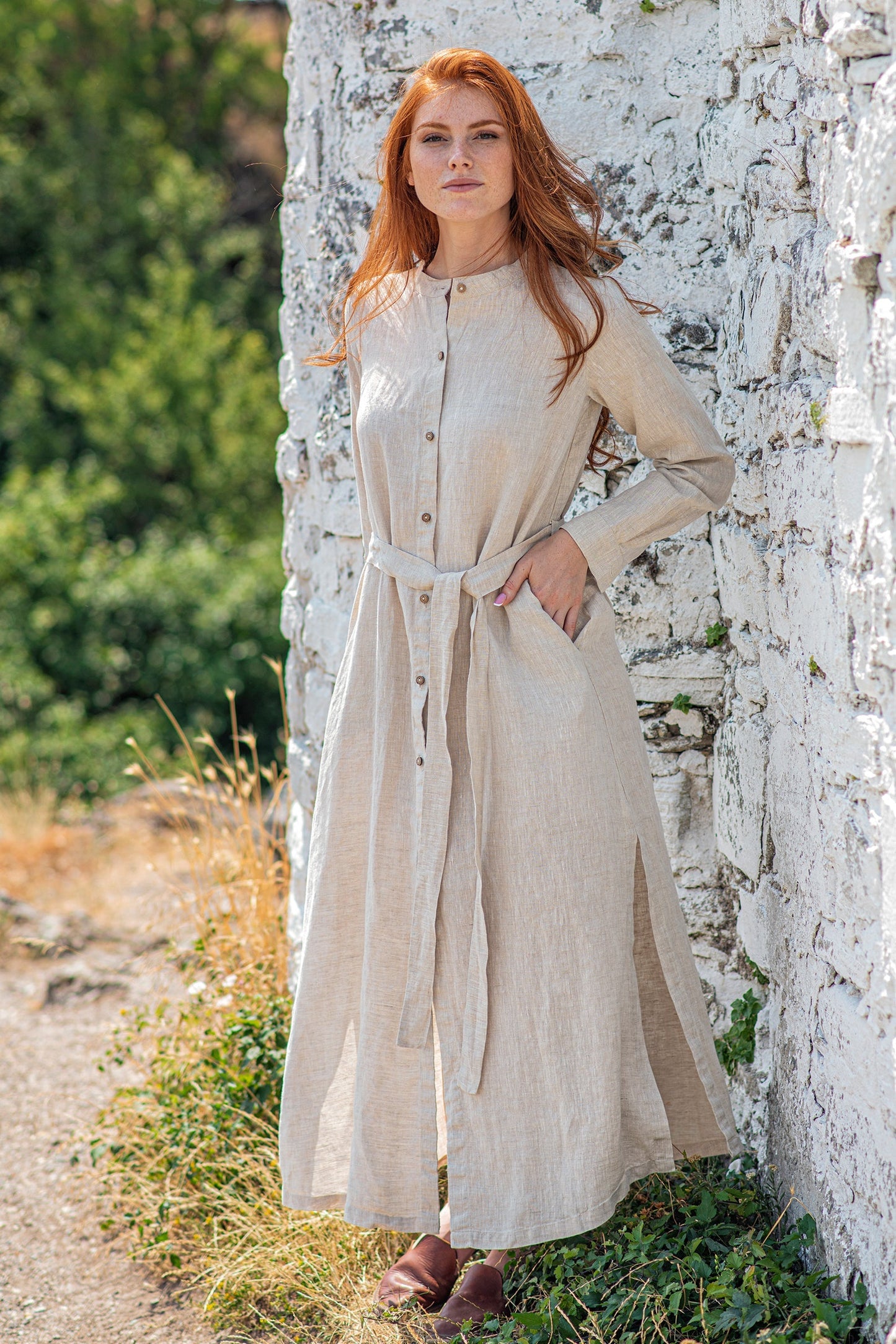 Woman wearing long sleeve linen shirt dress with front buttons and side slits standing outdoors