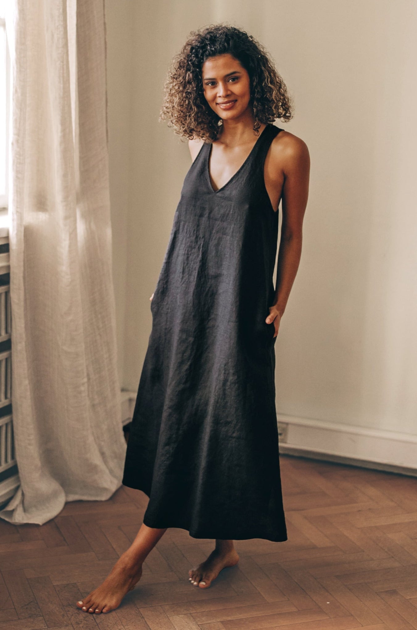 Woman wearing sleeveless black minimalist linen dress with V-neck and halter back indoors