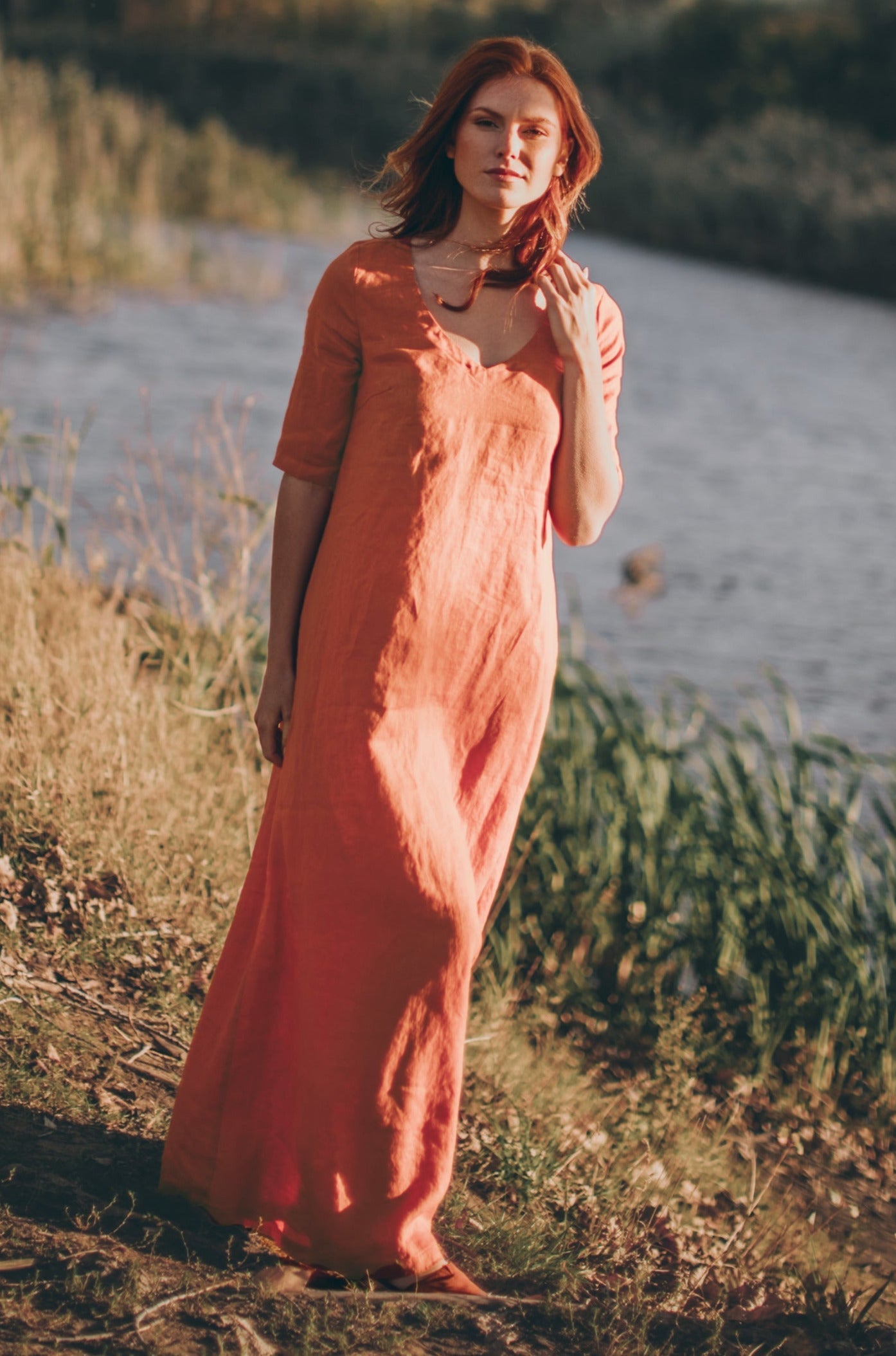 Woman wearing rust orange sleeved linen maxi dress outdoors by water