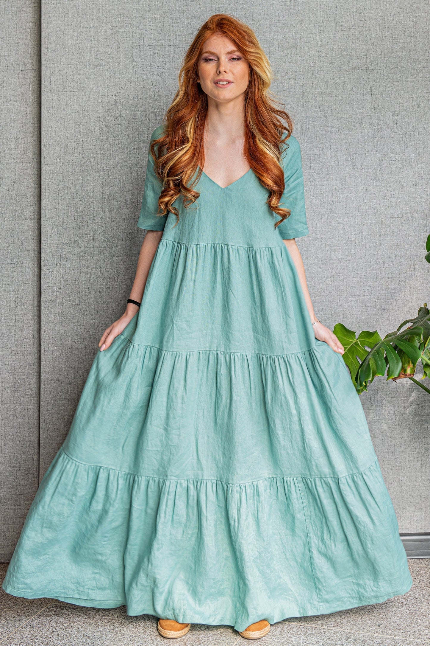 Woman wearing dusty turquoise bohemian linen dress with tiered skirt and V-neck standing indoors