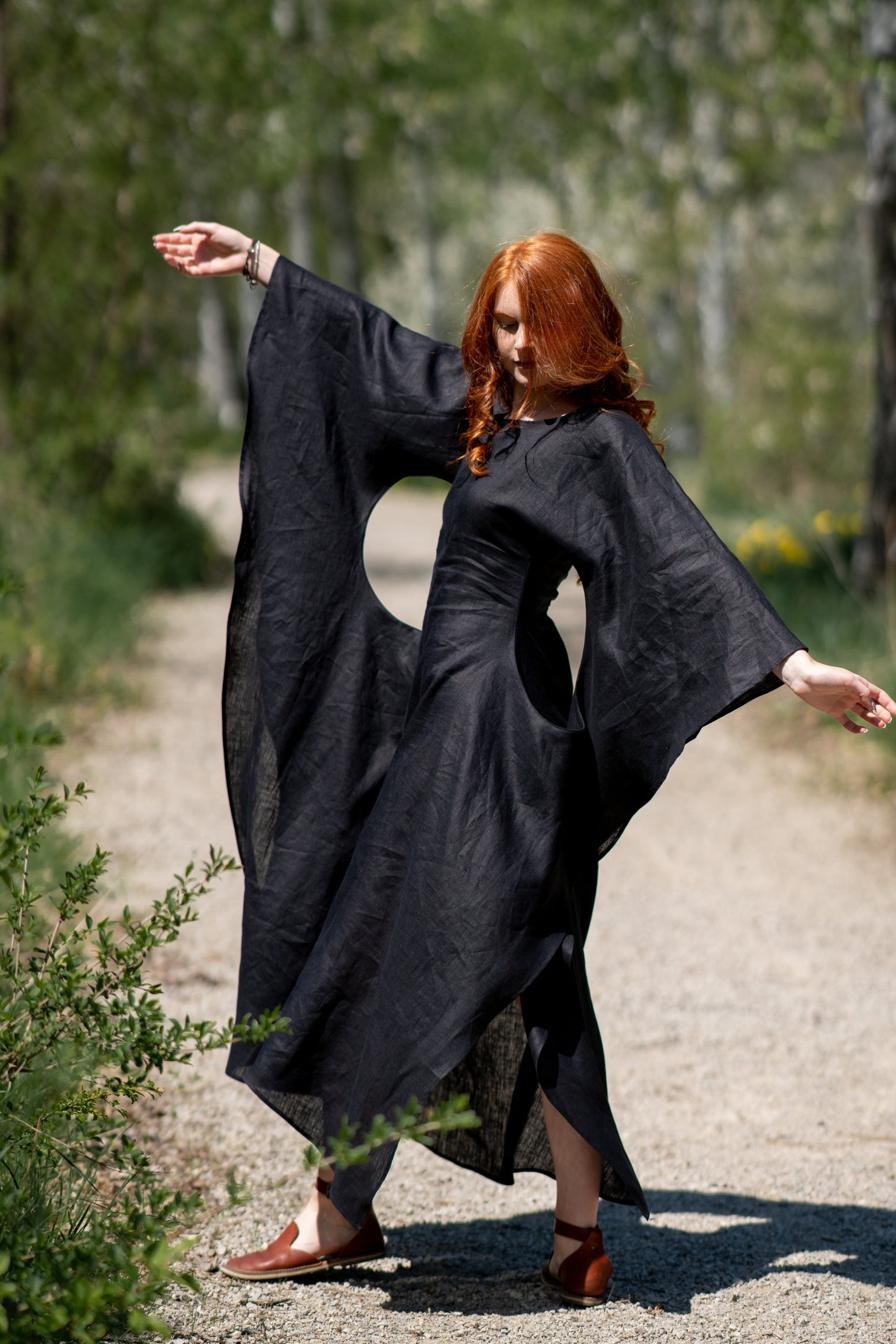 Woman wearing long black linen batwing dress outdoors with flowy sleeves and minimalist silhouette