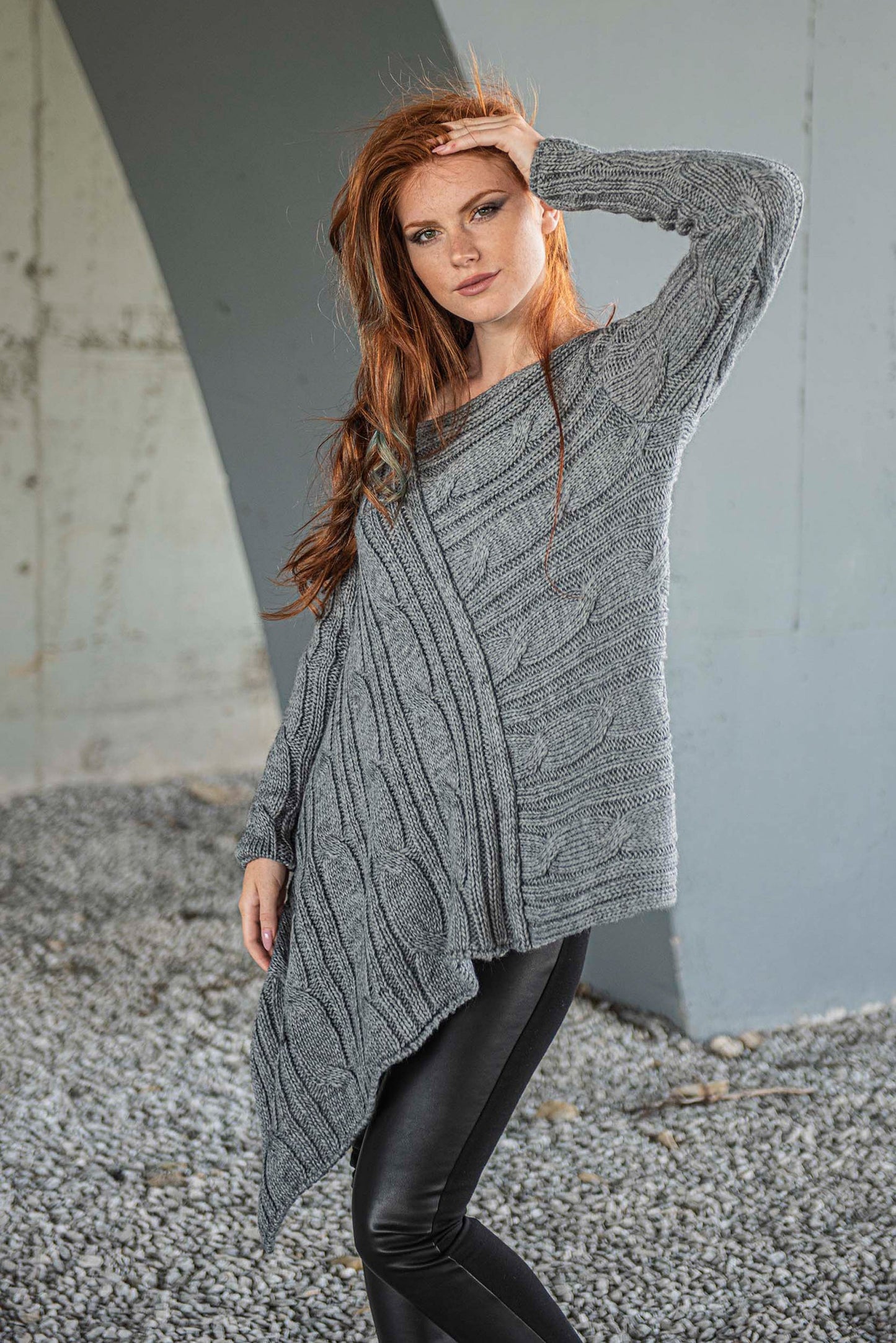 Woman wearing gray asymmetric knit sweater with multi-directional ribbing and oversized fit