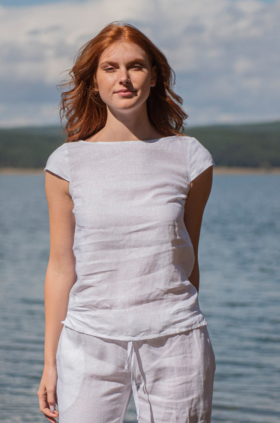 Woman wearing white linen top with cap sleeves by the water on a sunny day