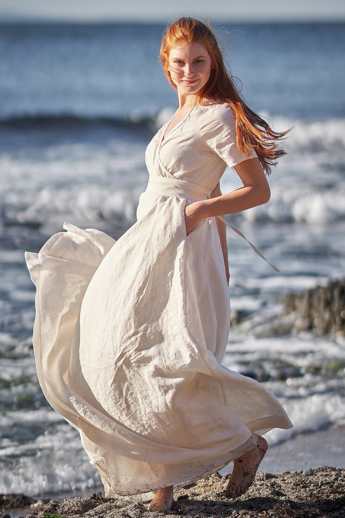 Woman wearing a creamy linen wrap dress with short sleeves and side pockets at the beach