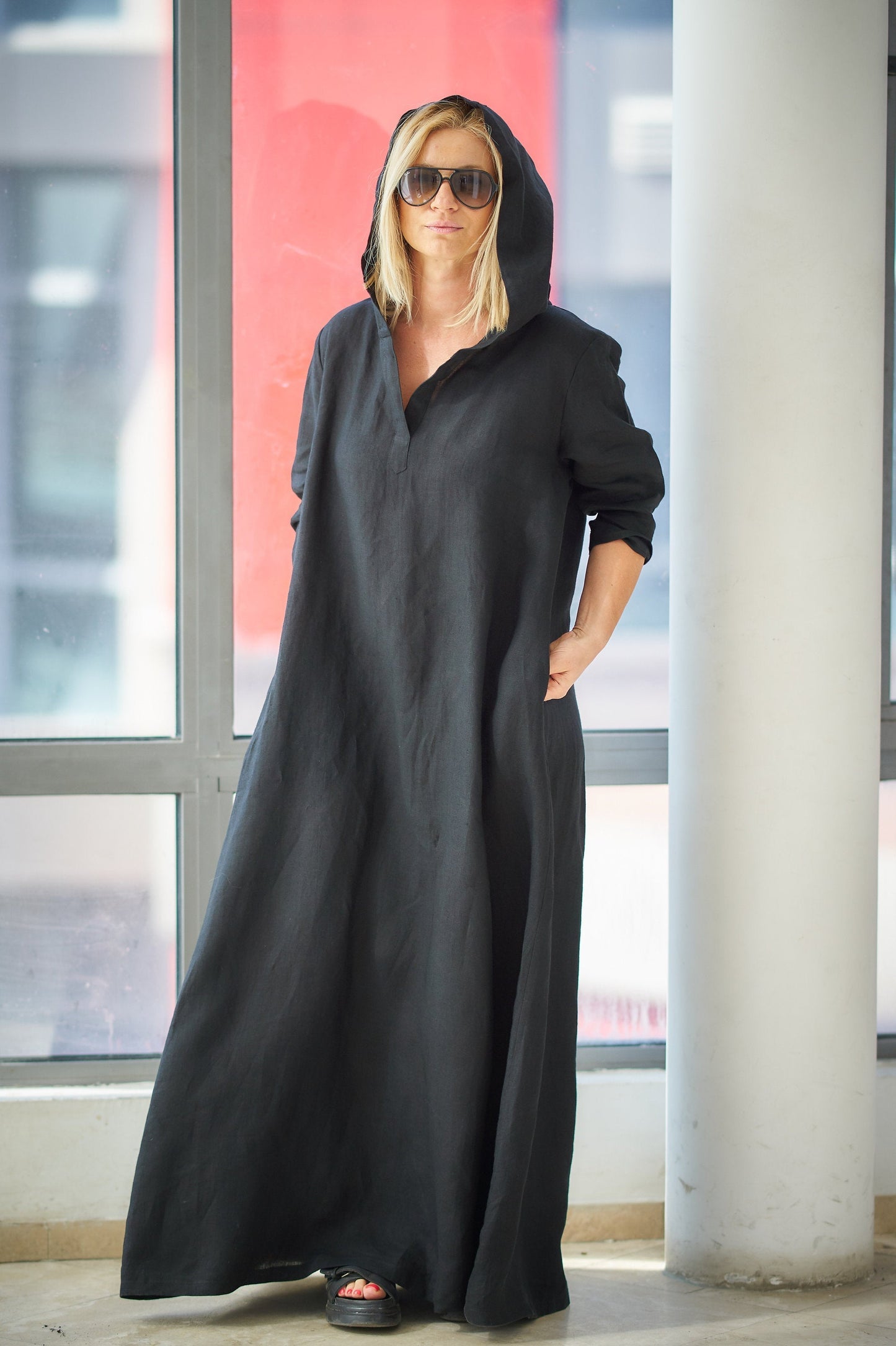 Woman wearing black hooded linen kaftan dress with pleated back and split neckline