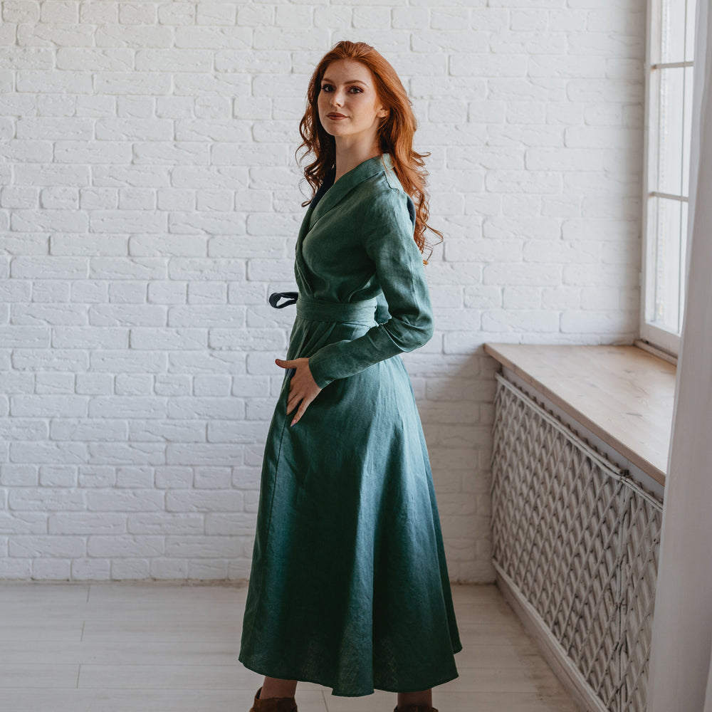 
                      
                        Woman in a green dress standing in a room with white brick walls and a window.
                      
                    