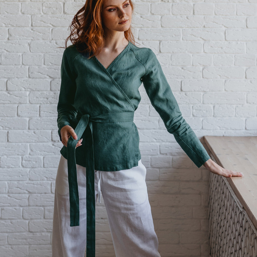 
                      
                        Woman wearing a green top and white pants against a white brick wall.
                      
                    