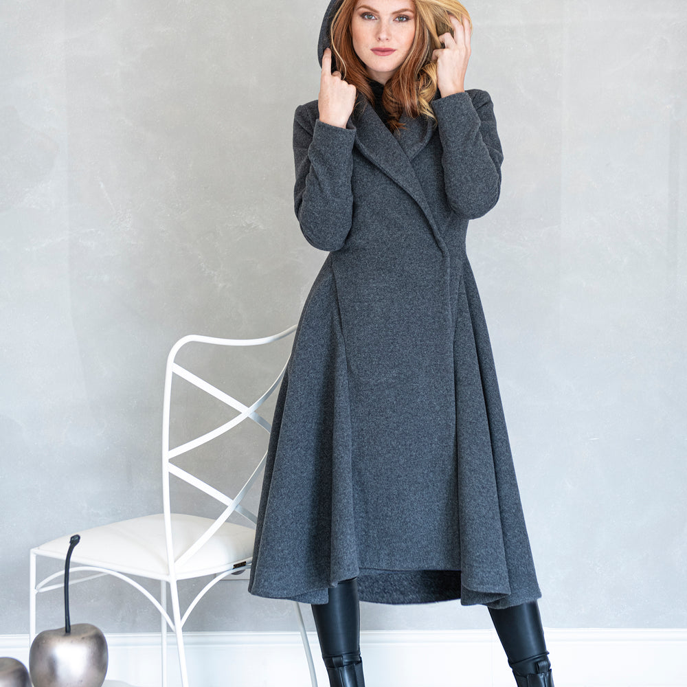 
                      
                        Woman wearing a gray wool coat standing in a room with a white chair and decorative apples.
                      
                    