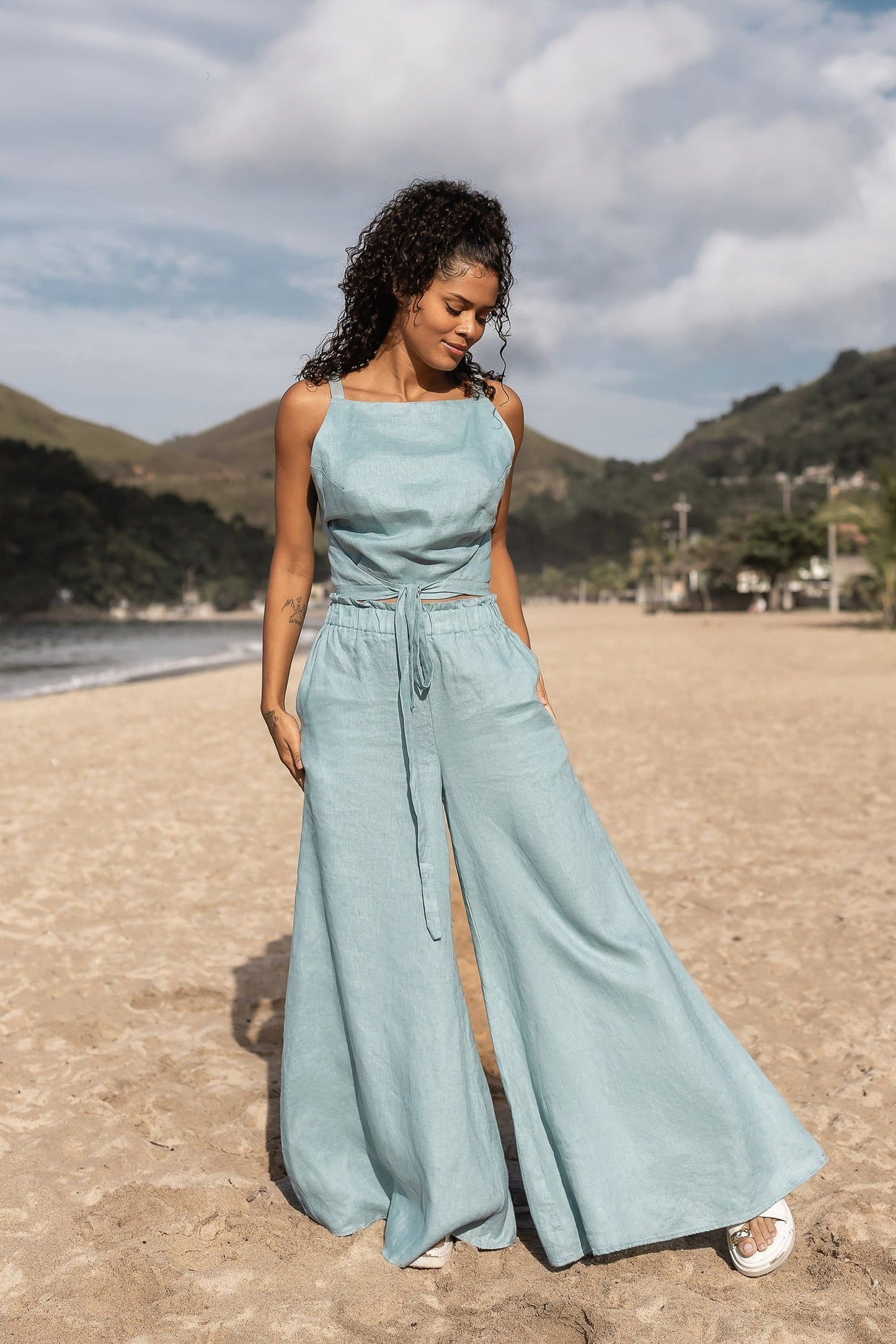 Woman wearing stylish linen wide leg pants with elastic waistband and side pockets standing against white background