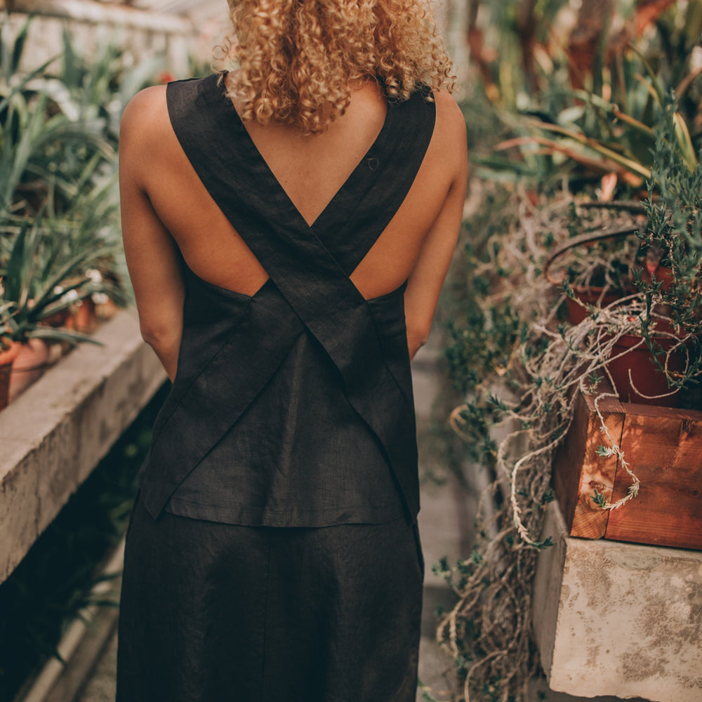 Cross-back linen top with V-neckline, made from 100% linen, displayed on model in a lush garden setting.