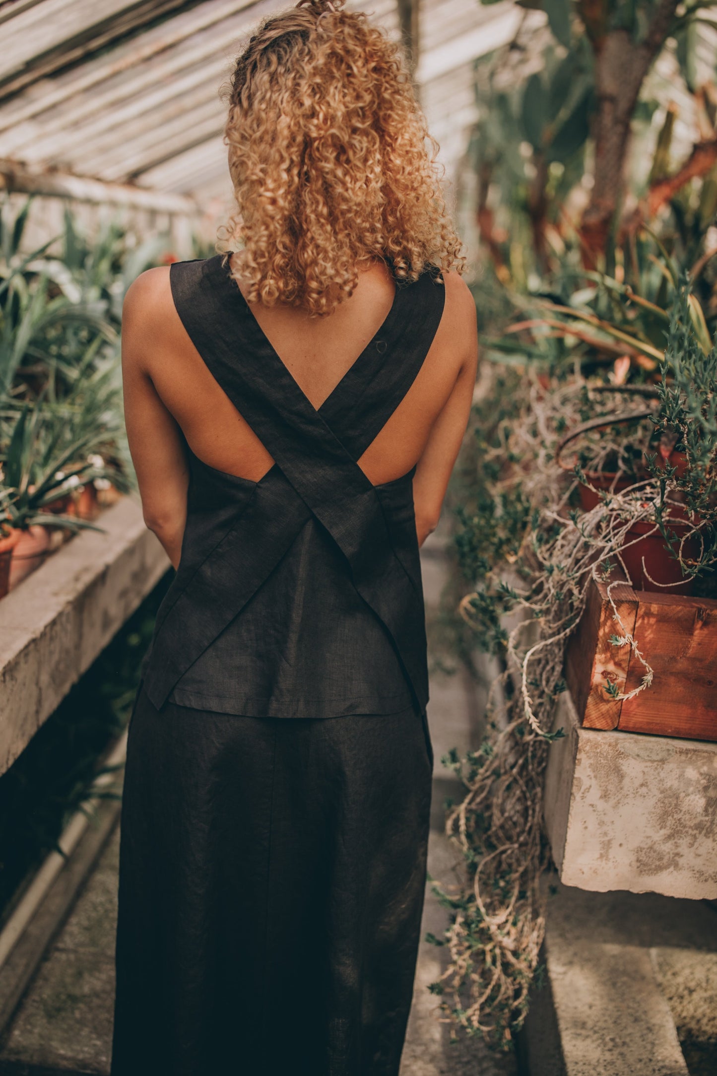 Cross-back linen top with V-neckline, made from 100% linen, displayed on model in a lush garden setting.