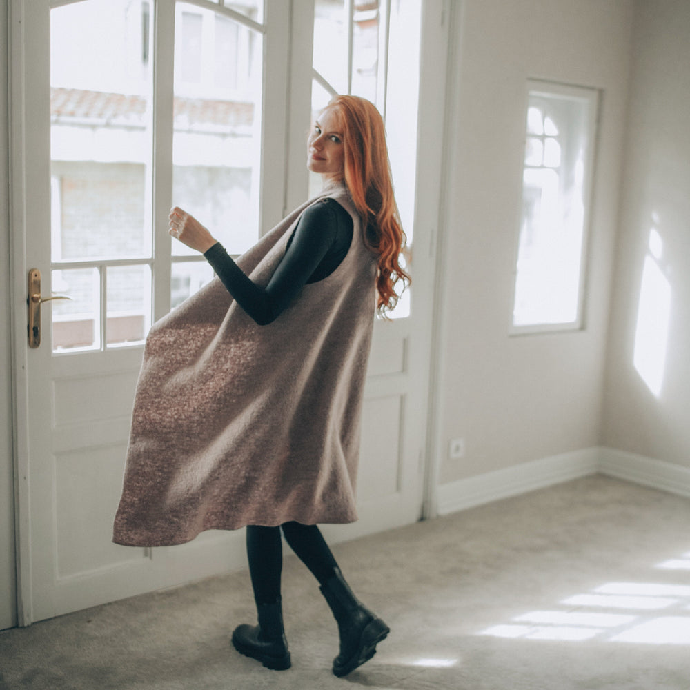 
                      
                        Woman standing in a room with large windows, wearing a long vest.
                      
                    
