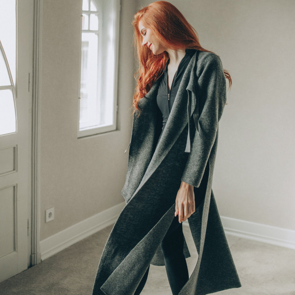 
                      
                        Woman wearing a long dark gray cardigan in a minimalistic room.
                      
                    