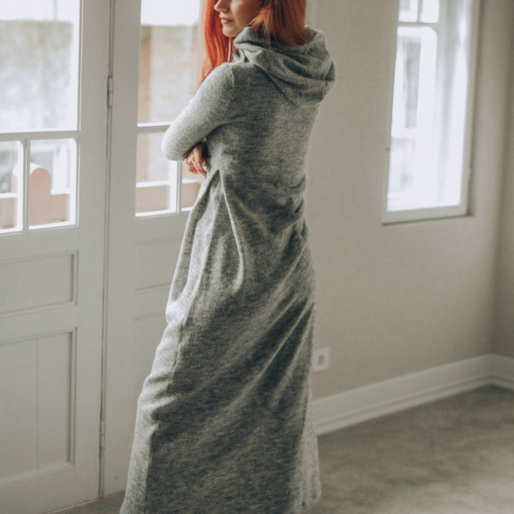 Woman wearing gray hooded knit dress with gathered side accent and black boots indoors
