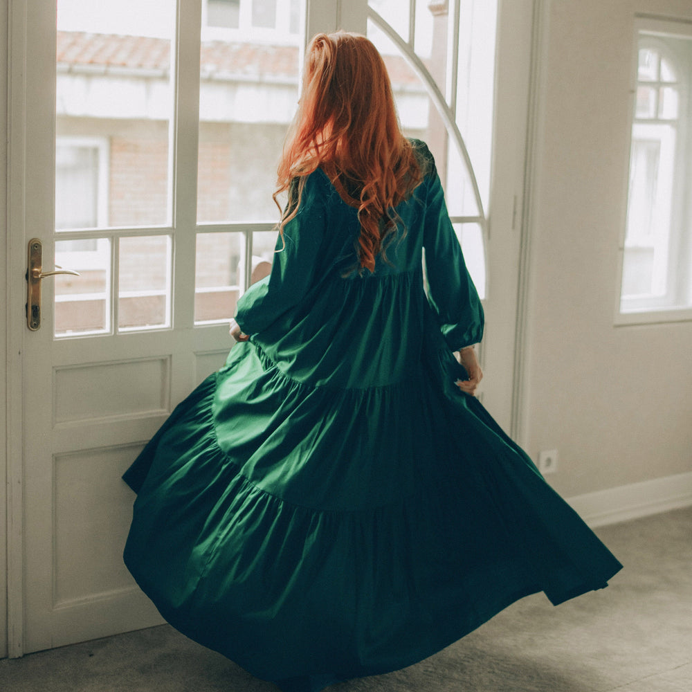 Woman in a green dress twirling in a room with large windows.