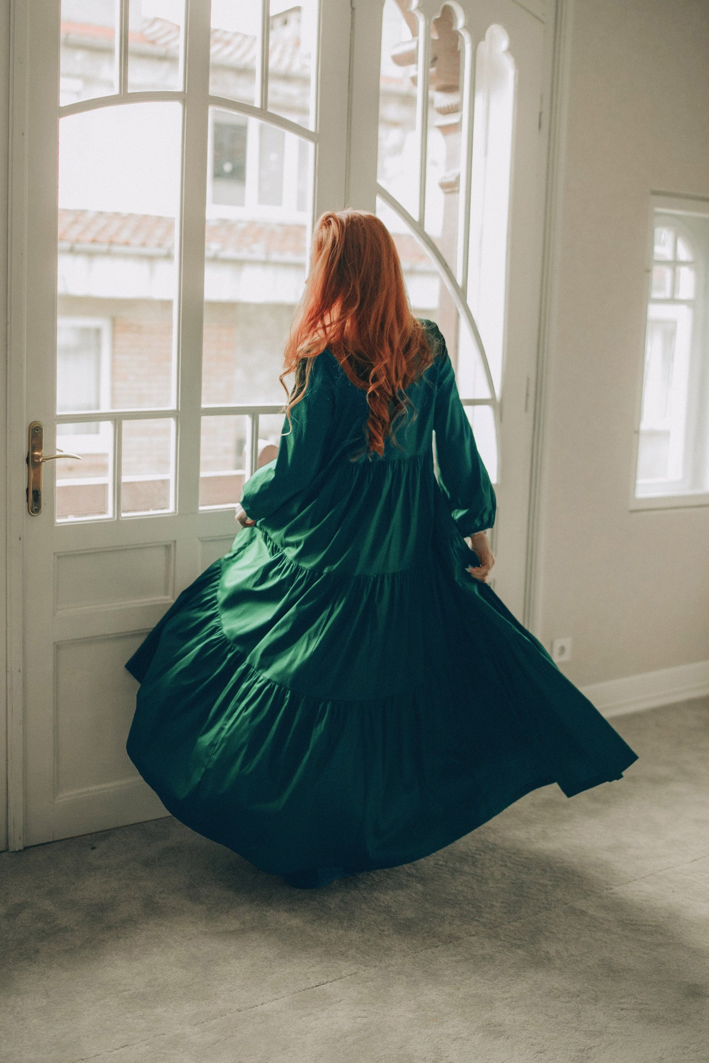 Woman in a green dress twirling in a room with large windows.