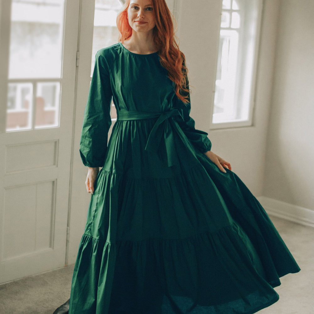 woman wearing green tiered cotton maxi dress with long sleeves and tie waist standing indoors