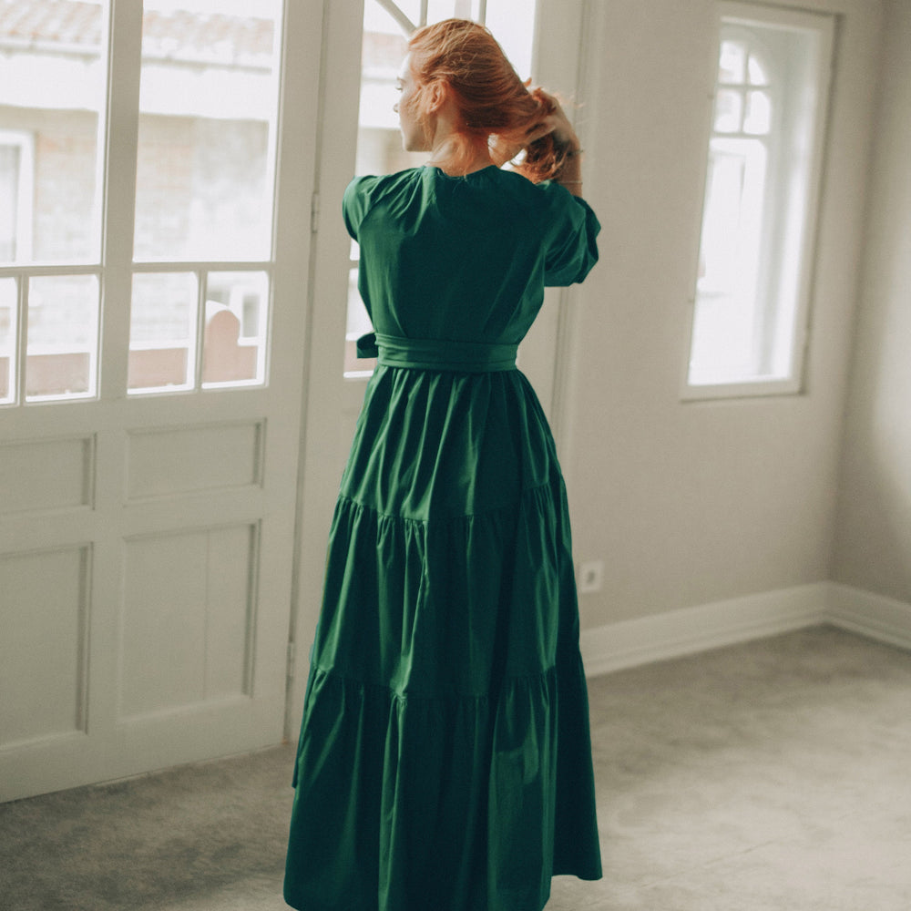 
                      
                        Woman in a green dress standing in a room with large windows.
                      
                    