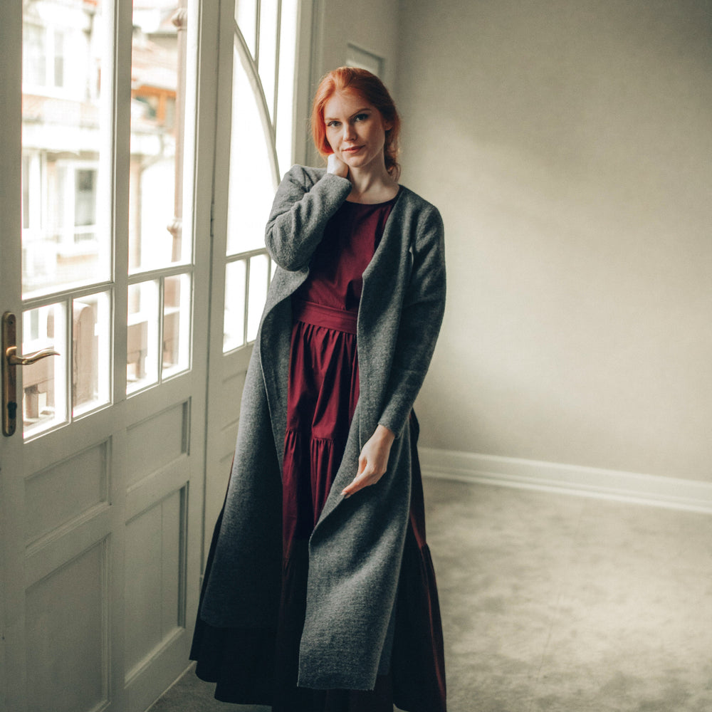 
                      
                        Woman wearing a long dark gray cardigan in a minimalistic room.
                      
                    