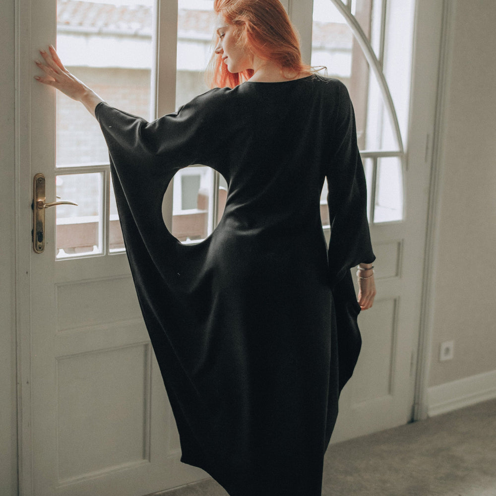 Woman wearing black batwing sleeve midi dress standing by a window