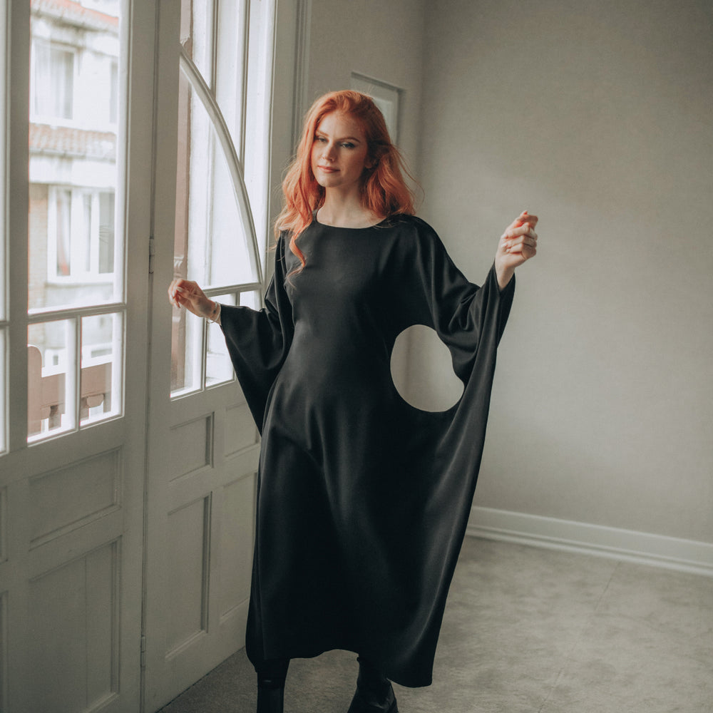 
                      
                        Woman wearing a black midi dress with a moon design in a room with large windows.
                      
                    