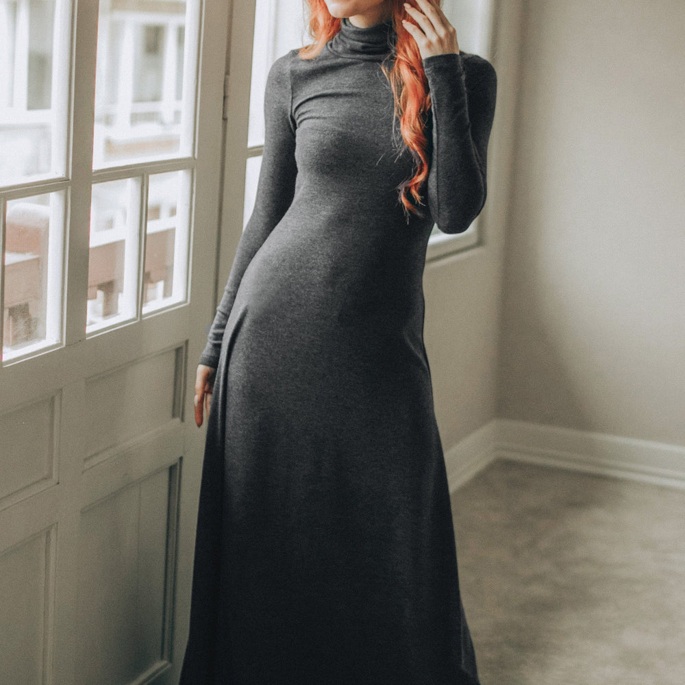 Woman wearing a fitted charcoal cotton maxi turtleneck dress with long sleeves near window