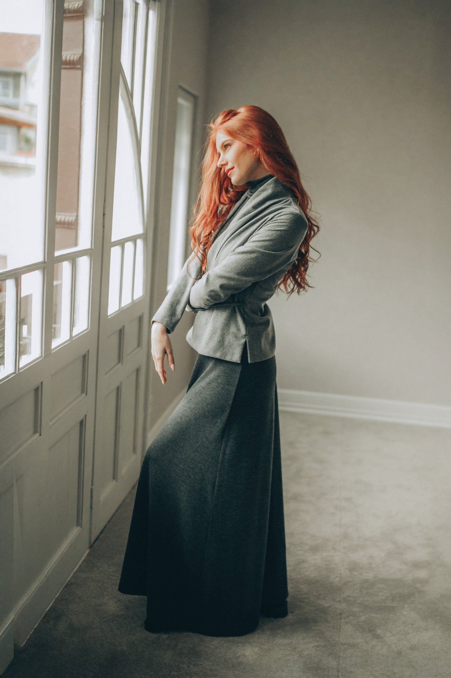 Woman in a gray cardigan standing in a room with large windows.
