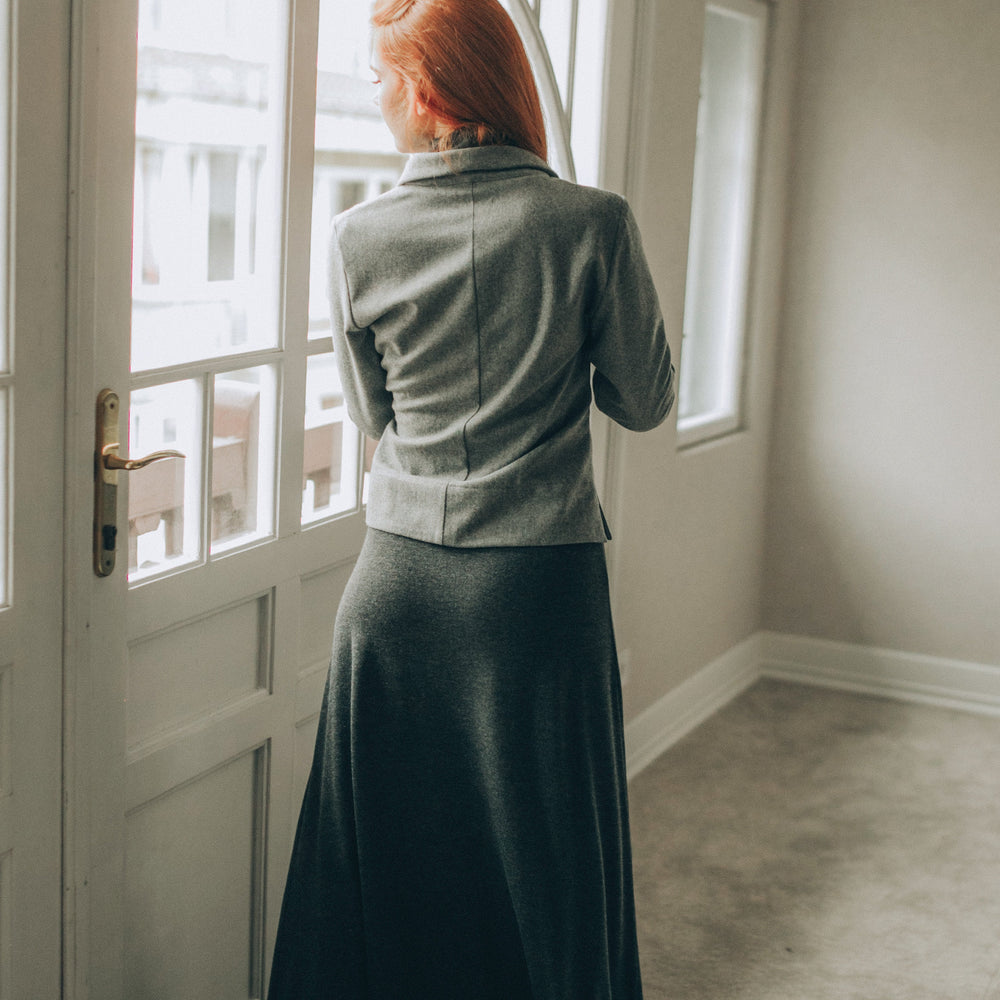 
                      
                        Woman in a gray wool cardigan tanding by a window in a well-lit room
                      
                    