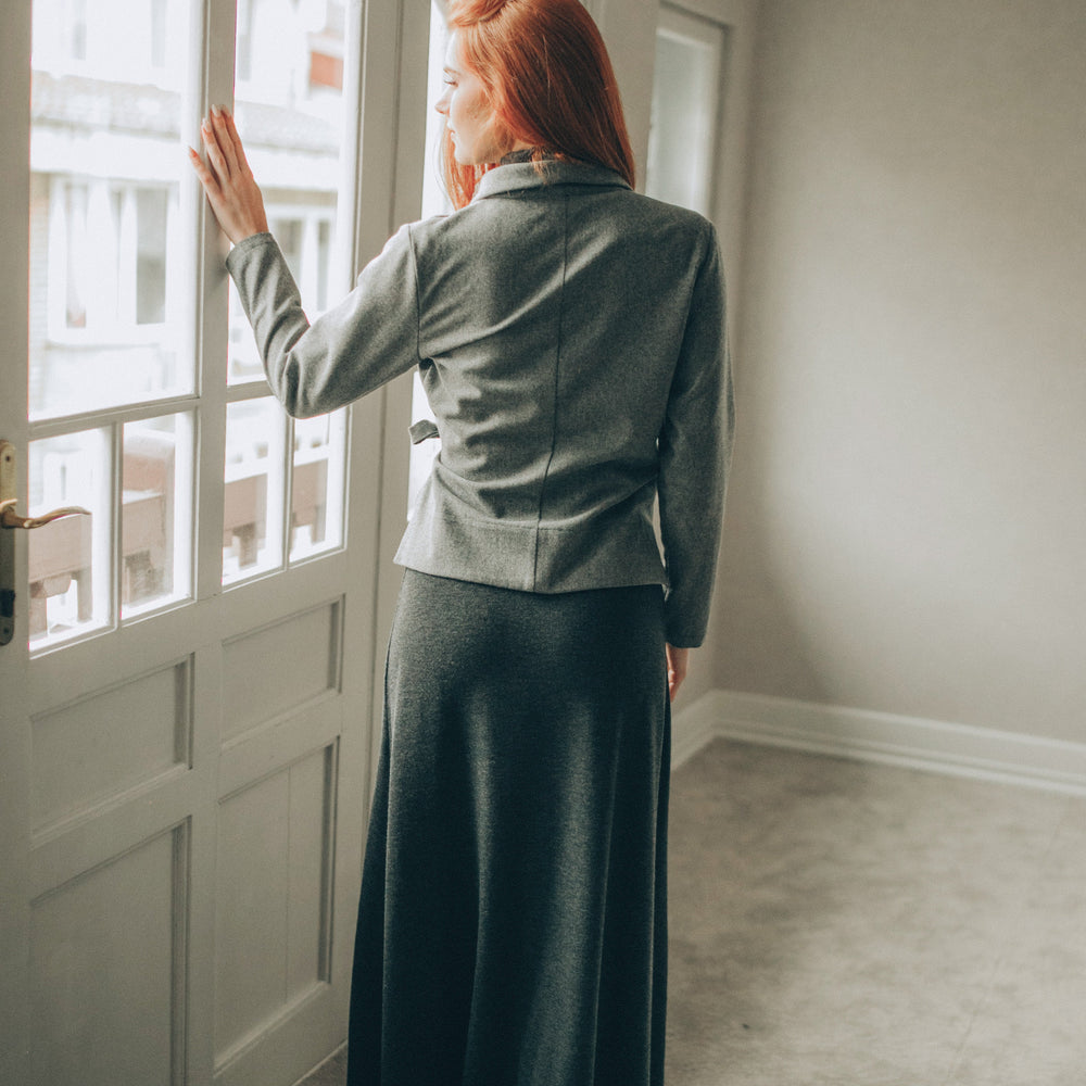 
                      
                        Woman in a gray wool cardigan tanding by a window in a well-lit room
                      
                    