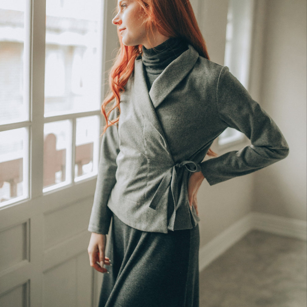 Woman wearing grey wool wrap cardigan with shawl collar standing by window