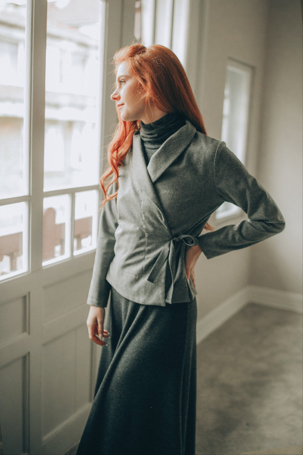 Woman wearing grey wool wrap cardigan with shawl collar standing by window
