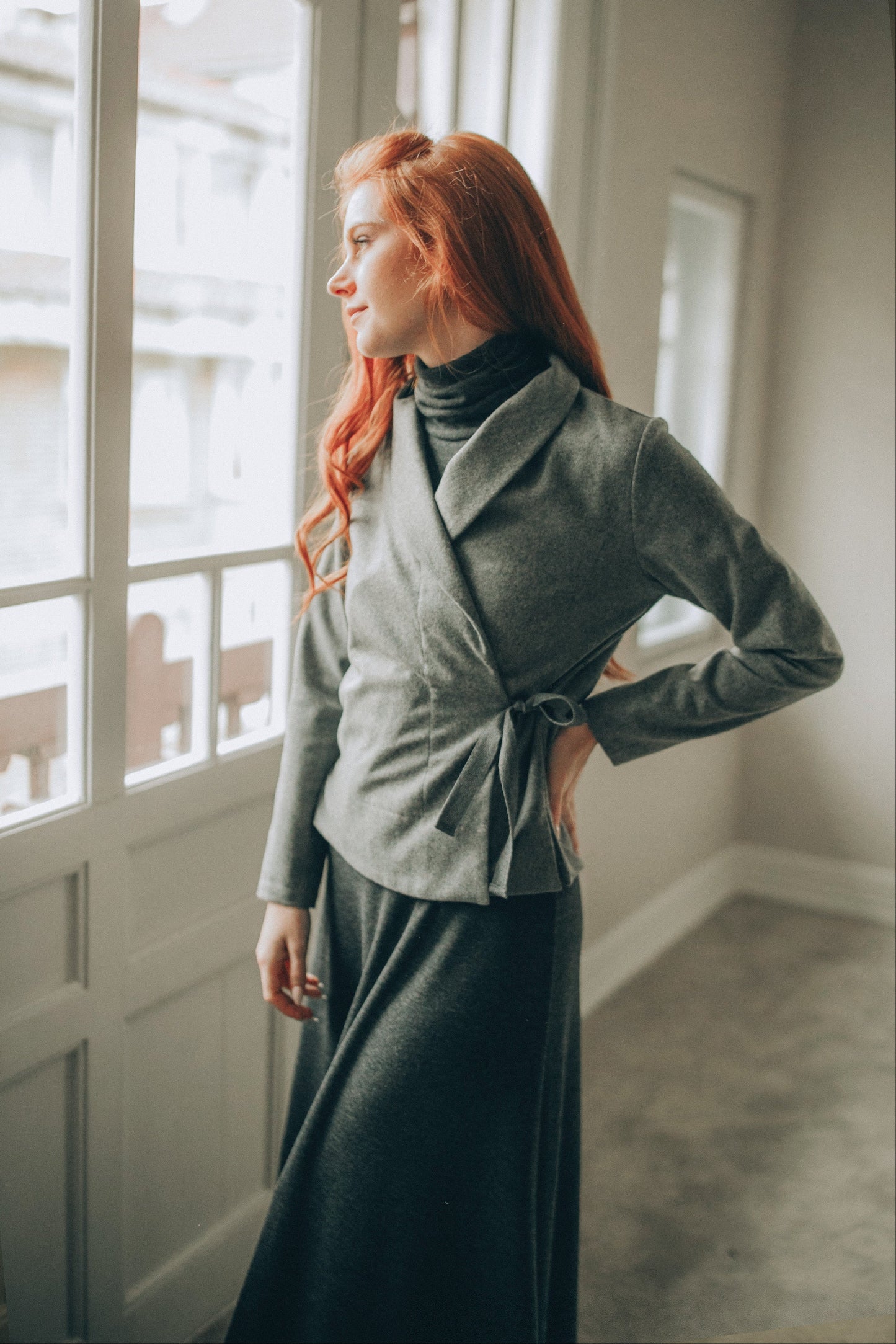 Woman wearing grey wool wrap cardigan with shawl collar standing by window