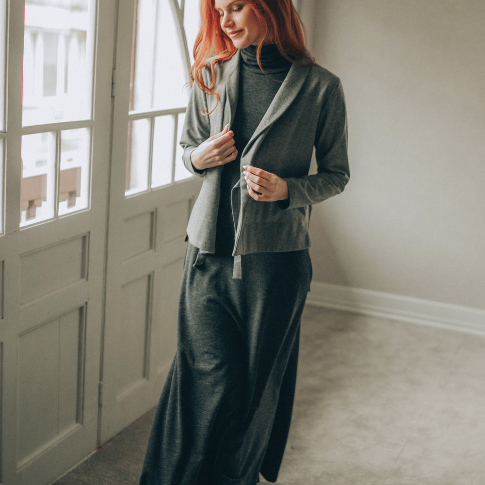 
                      
                        Woman in a gray wool cardigan tanding by a window in a well-lit room
                      
                    