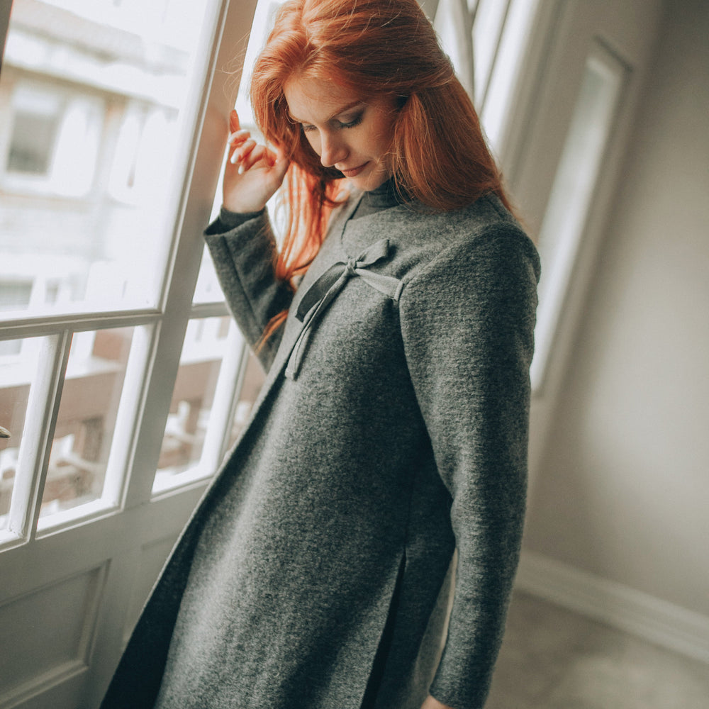 
                      
                        Woman wearing a long dark gray cardigan in a minimalistic room.
                      
                    