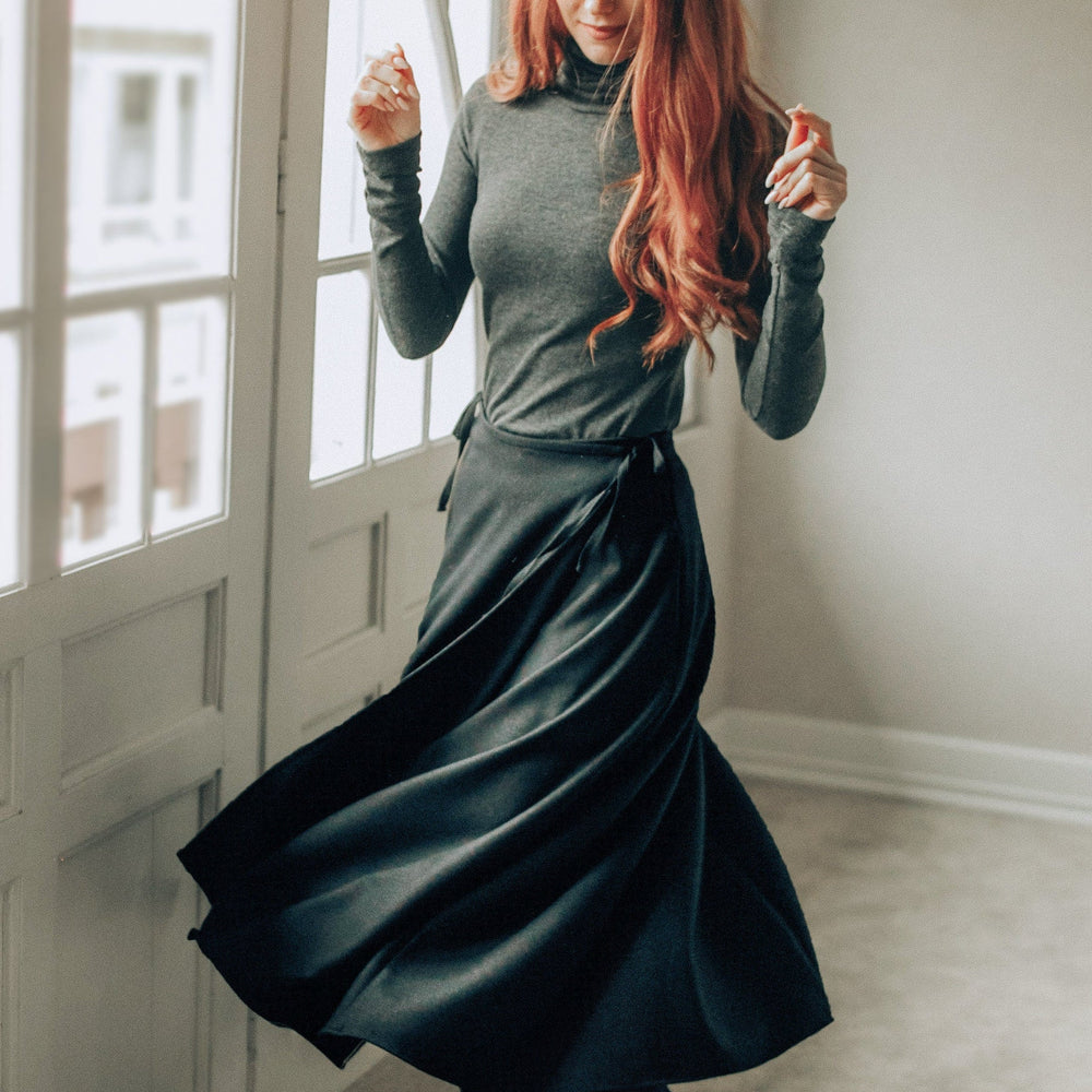 Woman wearing a black wool wrap maxi skirt with tie waist and long sleeves indoors