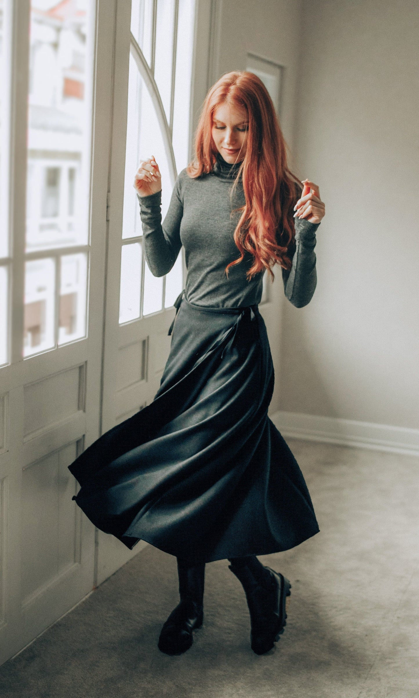 Woman wearing a black wool wrap maxi skirt with tie waist and long sleeves indoors