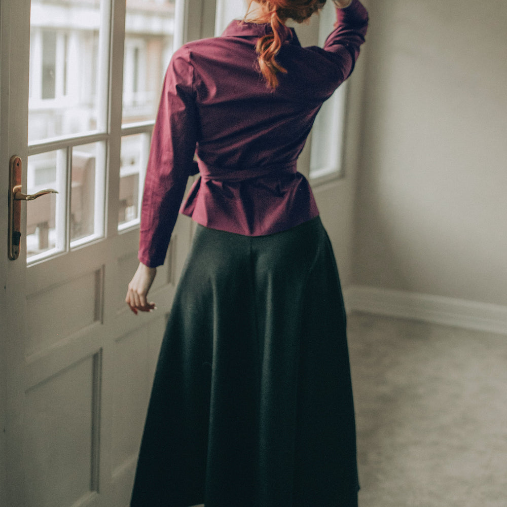 
                      
                        Woman in a burgundy wrap top and black skirt standing by a window 
                      
                    