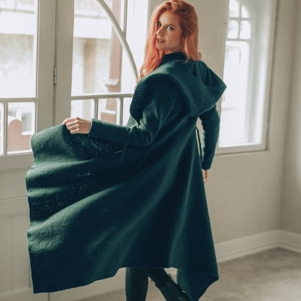 woman wearing emerald green asymmetrical wool cardigan coat with hood indoors