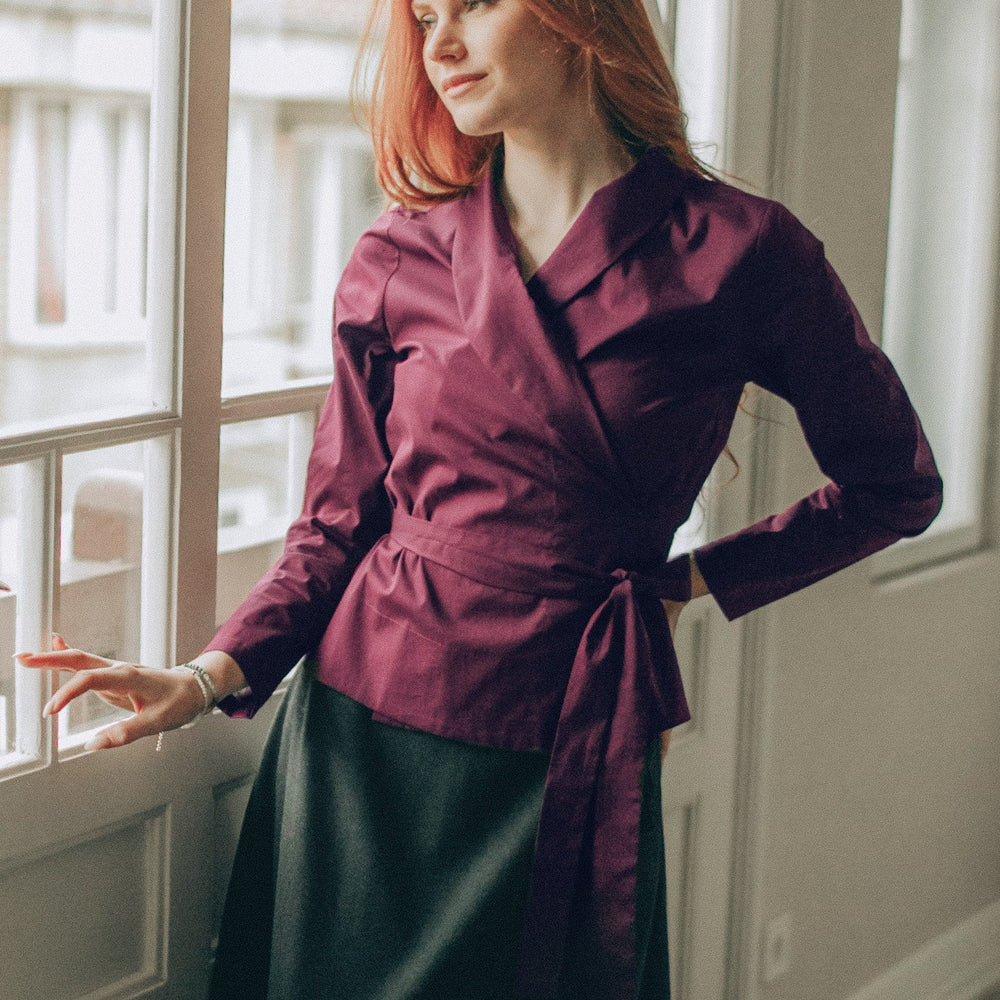 Burgundy cotton wrap top with shawl collar and adjustable tie waist worn by woman indoors