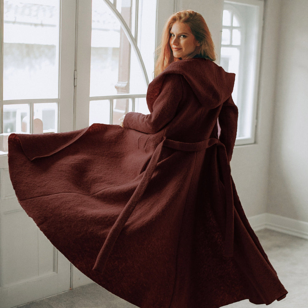 
                      
                        Woman wearing a flowing burgundy maxi wool hooded cardigan coat with an adjustable belt and hood indoors
                      
                    