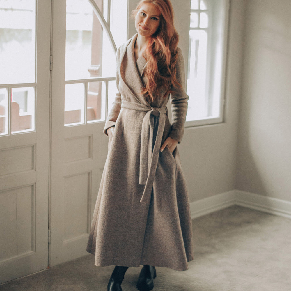 
                      
                        Woman in a long coat standing in a room with large windows.
                      
                    