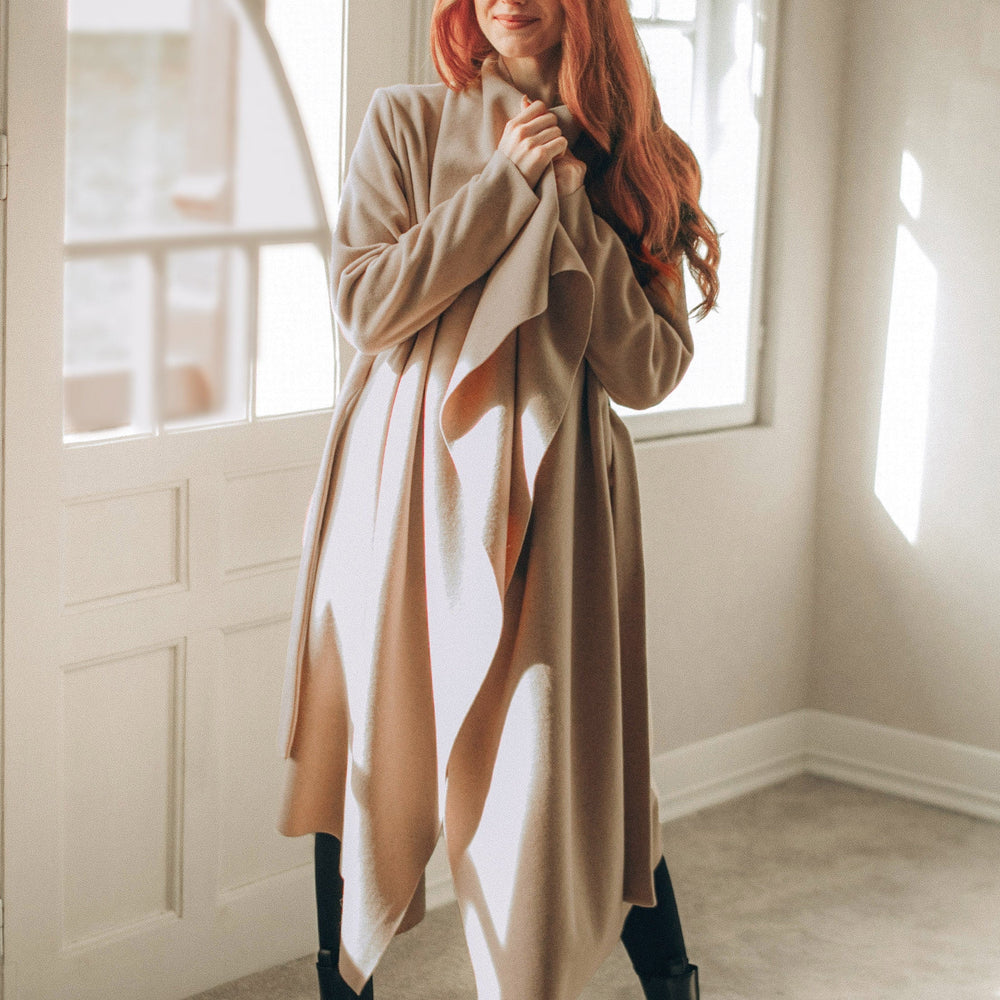 woman wearing powder beige wool cardigan coat with belt standing indoors near window