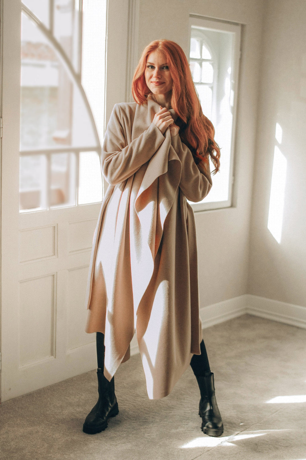 woman wearing powder beige wool cardigan coat with belt standing indoors near window