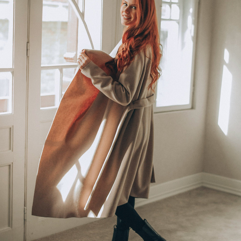 Woman with red hair standing in a sunlit room holding a coat